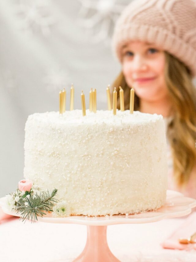 a white cake with gold candles sitting in front of a girl