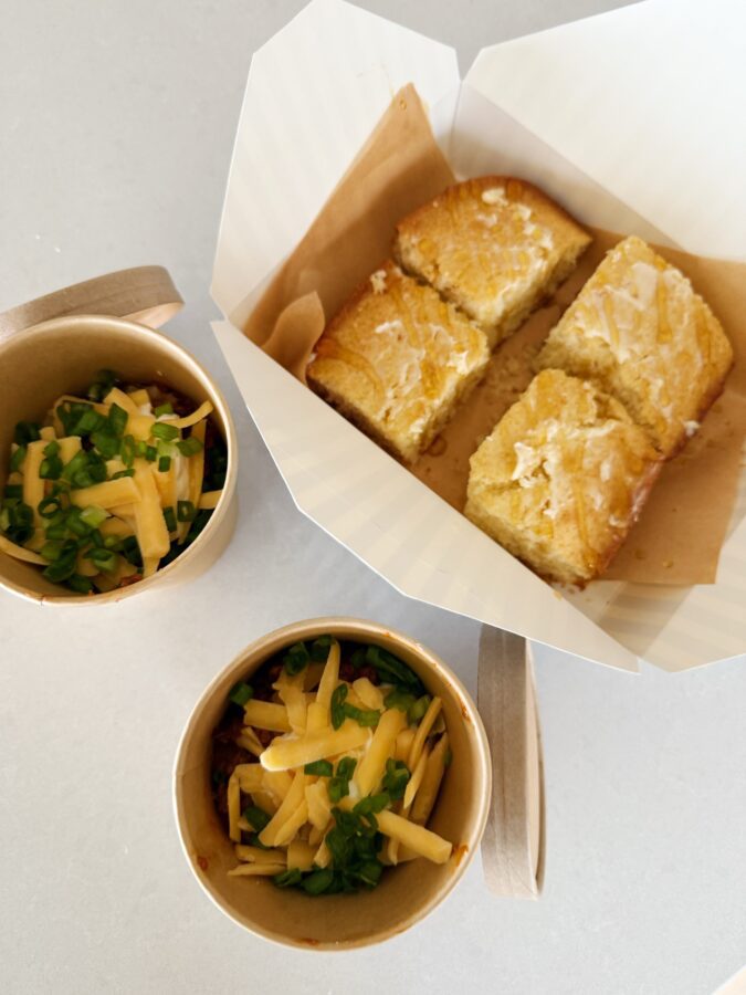 two bowls of chili with cheese and a batch of cornbread cut into squares