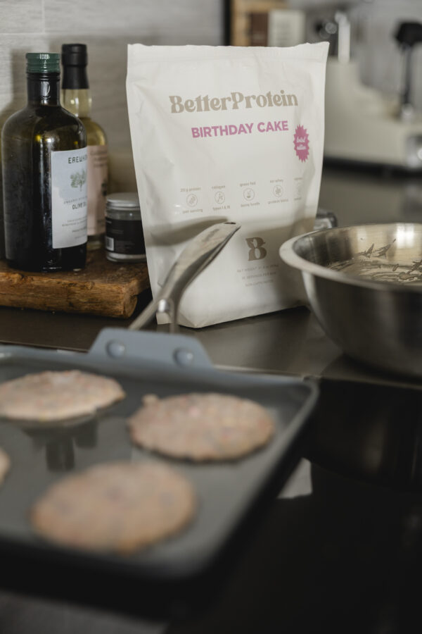 close up of pancakes on the griddle with protein powder in the background