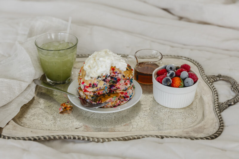 close up of a stack of sprinkle pancakes on tray with fruit